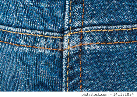 Blue denim fabric close up showing heavy stitching detail. Macro view of rugged jeans material with contrast thread. Textile background for fashion industry and clothing design concept Blue denim fabric close up showing heavy stitching detail. Macro view of rugged jeans material with contrast thread. Textile background for fashion industry and clothing design concept 141151054