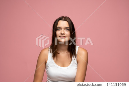Young brunette woman looking at camera with friendly expression, wearing a white tank top on a pink background Young brunette woman looking at camera with friendly expression, wearing a white tank top on a pink background 141151069