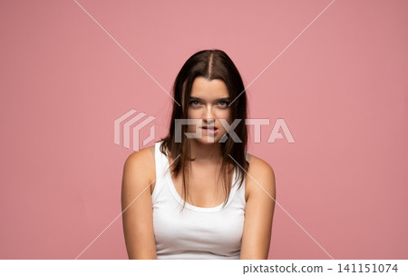 Young woman biting lower lip, looking at camera, conveying playful seduction and desire on pink background Young woman biting lower lip, looking at camera, conveying playful seduction and desire on pink background 141151074