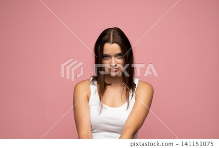 Young woman with smirk expression posing in white tank top against pink background, feeling self-assured Young woman with smirk expression posing in white tank top against pink background, feeling self-assured 141151075