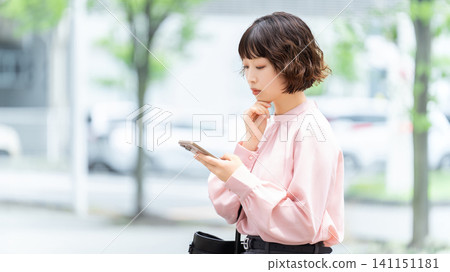 Woman/businesswoman thinking while looking at smartphone Woman/businesswoman thinking while looking at smartphone 141151181