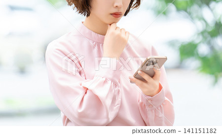 Woman/businesswoman thinking while looking at smartphone Woman/businesswoman thinking while looking at smartphone 141151182