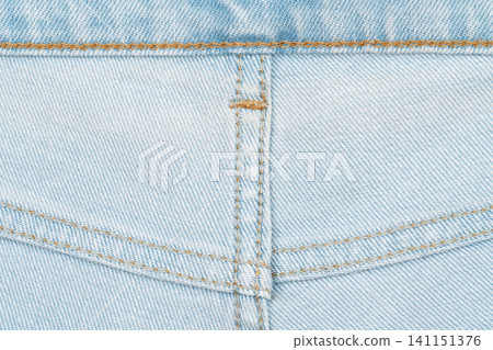 Close up of light blue denim fabric with golden stitching and pocket detail Close up of light blue denim fabric with golden stitching and pocket detail 141151376