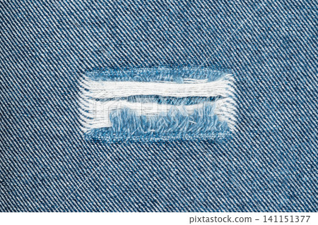 Torn denim fabric with frayed edges and exposed white threads 141151377