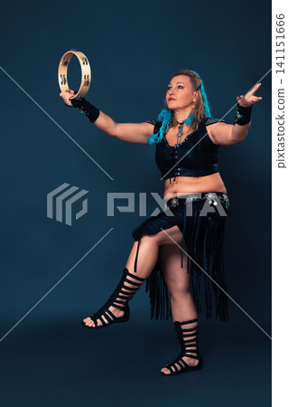 Extraordinary dancer stands on one leg in time with rhythmic strike of tambourine held in one hand Extraordinary dancer stands on one leg in time with rhythmic strike of tambourine held in one hand 141151666