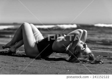 Woman with eyes closed lying on sand at beach. Black and white vintage photo style with noise Woman with eyes closed lying on sand at beach. Black and white vintage photo style with noise 141152122