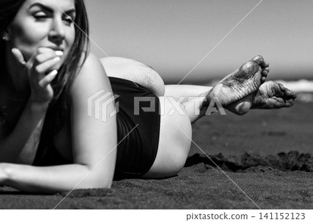 Woman lying on sand at beach. Black and white vintage image of sunbathing female in swimsuit Woman lying on sand at beach. Black and white vintage image of sunbathing female in swimsuit 141152123