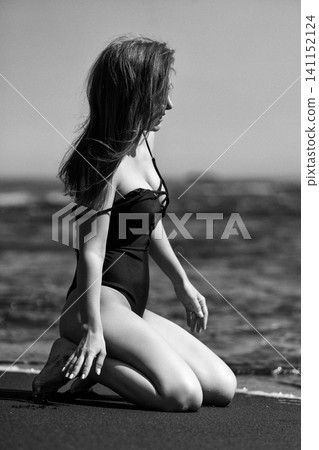 Sensuality woman in swimsuit kneeling on sandy beach. Black and white with analog grainy effect Sensuality woman in swimsuit kneeling on sandy beach. Black and white with analog grainy effect 141152124