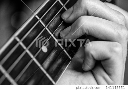 Woman playing guitar. Closeup of hand on fretboard pressing string to play chord. Black and white Woman playing guitar. Closeup of hand on fretboard pressing string to play chord. Black and white 141152351