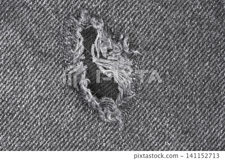 Torn denim fabric with frayed hole on textured gray background Torn denim fabric with frayed hole on textured gray background 141152713