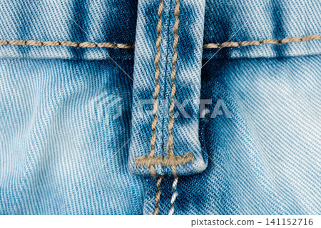 Blue jean belt loop detail closeup. Denim fabric texture with yellow stitching. Durable cotton clothing material and garment construction. Macro shot of blue pants for apparel design Blue jean belt loop detail closeup. Denim fabric texture with yellow stitching. Durable cotton clothing material and garment construction. Macro shot of blue pants for apparel design 141152716
