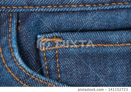 Closeup of blue denim fabric with orange stitching and pocket detail 141152723