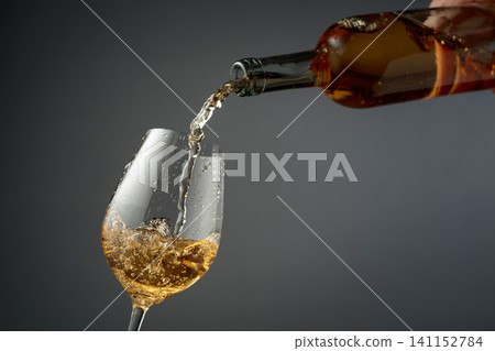 Pouring white wine from a bottle into a glass. Pouring white wine from a bottle into a glass. 141152784