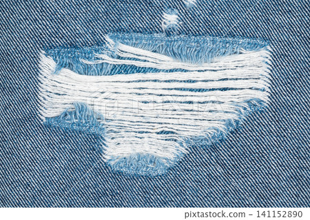 Torn denim fabric with frayed white threads and blue weave texture 141152890