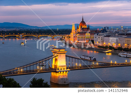 A breathtaking view of the Parliament Building and the Széchenyi Chain Bridge illuminated on the Danube River at sunset in Budapest, Hungary. A breathtaking view of the Parliament Building and the Széchenyi Chain Bridge illuminated on the Danube River at sunset in Budapest, Hungary. 141152946