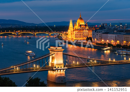 A stunning night view of the Parliament building and the Széchenyi Chain Bridge illuminated on the Danube River during the blue hour in Budapest, Hungary. 141152951