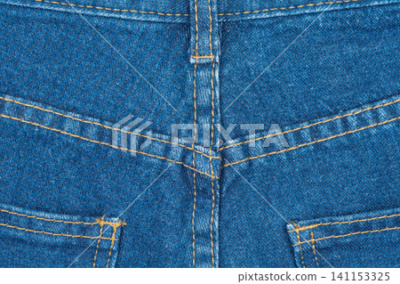 Blue jeans back pocket and yoke seam detail. Denim fabric texture background with yellow stitching Blue jeans back pocket and yoke seam detail. Denim fabric texture background with yellow stitching 141153325