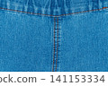 Blue denim fabric texture with symmetrical orange stitching and seam 141153334