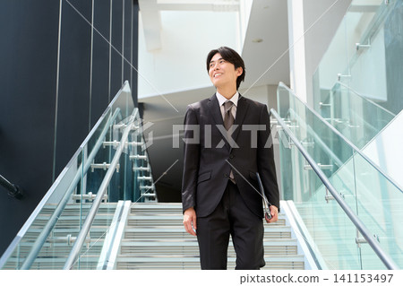 一名亞洲商人正走上辦公大樓的樓梯。 141153497