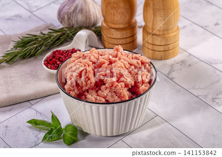 Raw minced chicken or turkey in a bowl with fresh herbs and spices on a kitchen counter 141153842