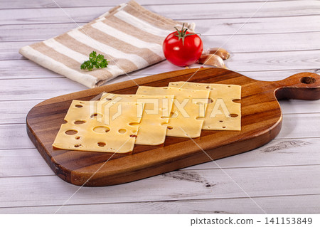 Sliced cheese with holes on wooden board with fresh tomato and garlic Sliced cheese with holes on wooden board with fresh tomato and garlic 141153849