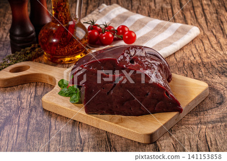 Raw beef liver on wooden cutting board with fresh herbs and cherry tomatoes Raw beef liver on wooden cutting board with fresh herbs and cherry tomatoes 141153858