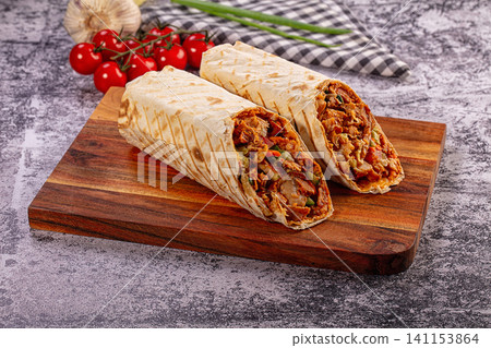 Two fresh shawarma wraps with meat and vegetables on rustic wooden cutting board Two fresh shawarma wraps with meat and vegetables on rustic wooden cutting board 141153864