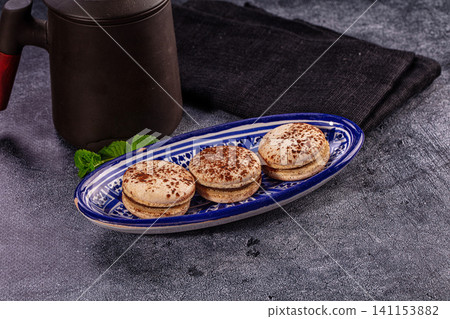 Three tiramisu macarons on blue ceramic plate with coffee pot Three tiramisu macarons on blue ceramic plate with coffee pot 141153882