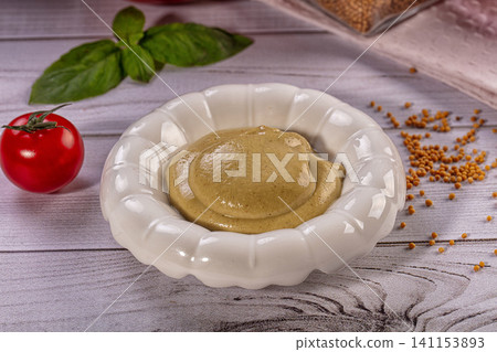 Mustard in white bowl with basil and tomato on wooden table Mustard in white bowl with basil and tomato on wooden table 141153893