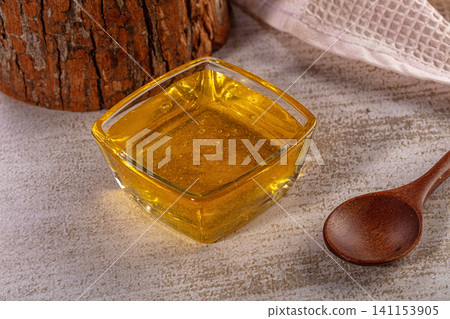 Fresh golden honey in square glass bowl with wooden spoon and log background Fresh golden honey in square glass bowl with wooden spoon and log background 141153905