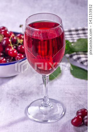 Red cherry juice in wine glass with fresh cherries and green leaves on light textured surface Red cherry juice in wine glass with fresh cherries and green leaves on light textured surface 141153932