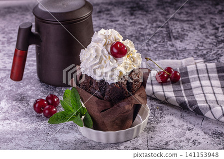 Chocolate cupcake with whipped cream and cherry on rustic table Chocolate cupcake with whipped cream and cherry on rustic table 141153948