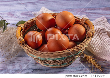 Brown eggs in woven basket on rustic wooden surface with wheat and cloth Brown eggs in woven basket on rustic wooden surface with wheat and cloth 141153950