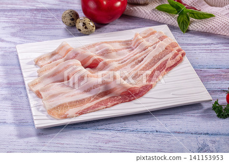 Raw bacon strips on white plate with tomato and quail eggs Raw bacon strips on white plate with tomato and quail eggs 141153953