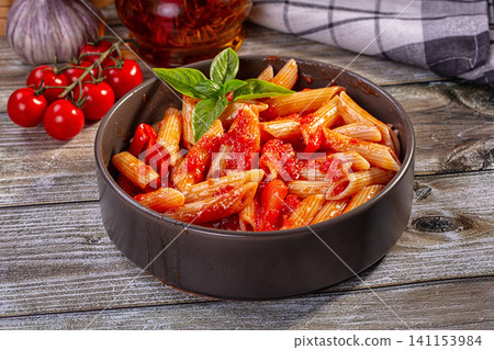 Penne pasta with tomato sauce and basil in dark bowl on rustic wood table Penne pasta with tomato sauce and basil in dark bowl on rustic wood table 141153984