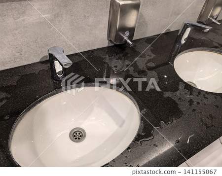 Wet black granite countertop with white sinks and chrome faucets closeup 141155067