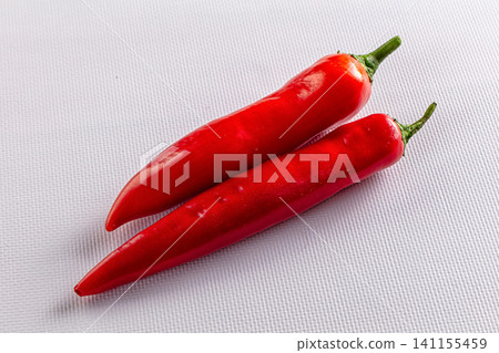 Two red chili peppers on white textured surface 141155459