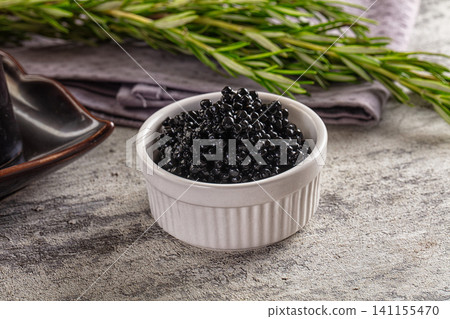 Black caviar in white ramekin with rosemary sprig on textured surface Black caviar in white ramekin with rosemary sprig on textured surface 141155470