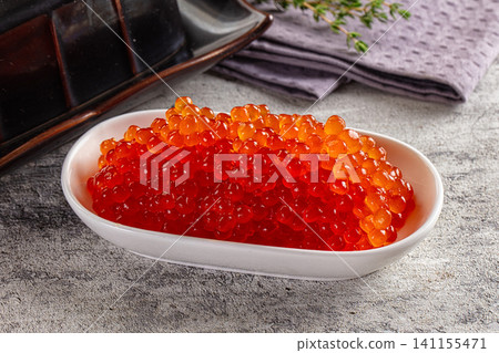 Vibrant red caviar in white ceramic bowl on textured gray surface with green herb garnish Vibrant red caviar in white ceramic bowl on textured gray surface with green herb garnish 141155471