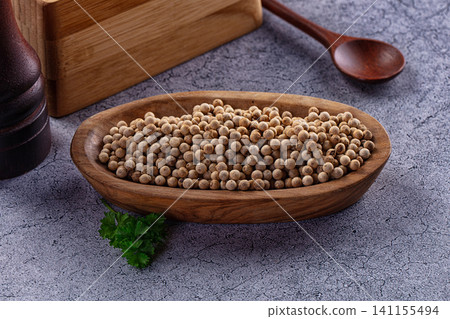 White peppercorns in wooden bowl with parsley and spoon on textured surface White peppercorns in wooden bowl with parsley and spoon on textured surface 141155494
