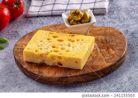Swiss cheese block with holes on wooden board with olives and tomatoes Swiss cheese block with holes on wooden board with olives and tomatoes 141155503