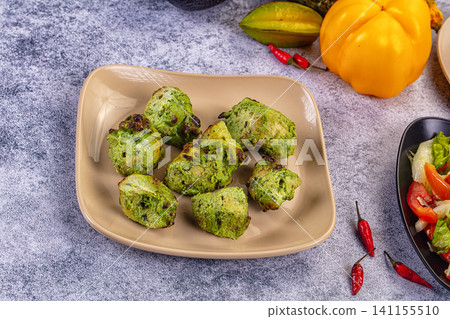 Mint chicken tikka pieces on beige plate with chili peppers and yellow pepper Mint chicken tikka pieces on beige plate with chili peppers and yellow pepper 141155510