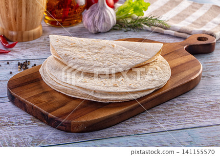 Stack of fresh tortillas on a wooden cutting board with garlic and herbs 141155570