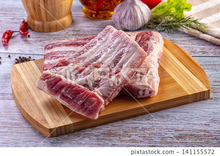 Fresh raw pork ribs on a bamboo cutting board surrounded by garlic, peppers, and herbs for cooking Fresh raw pork ribs on a bamboo cutting board surrounded by garlic, peppers, and herbs for cooking 141155572
