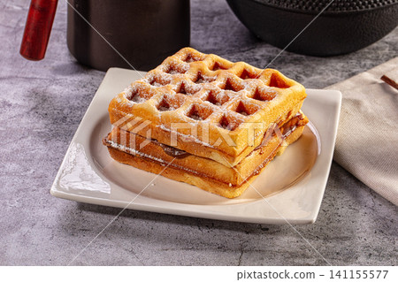 A stack of golden Belgian waffles filled with chocolate spread and dusted with powdered sugar on a white plate A stack of golden Belgian waffles filled with chocolate spread and dusted with powdered sugar on a white plate 141155577