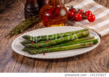 Fresh green asparagus spears on white plate with cherry tomatoes and oil bottle on rustic wood table Fresh green asparagus spears on white plate with cherry tomatoes and oil bottle on rustic wood table 141155627