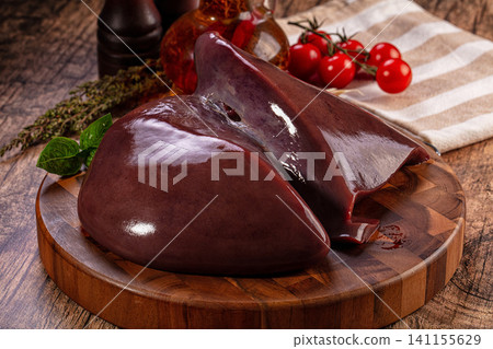 Raw beef liver on wooden cutting board with cherry tomatoes and herbs Raw beef liver on wooden cutting board with cherry tomatoes and herbs 141155629