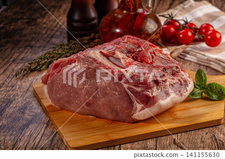 Raw pork shoulder on wooden cutting board with herbs and cherry tomatoes Raw pork shoulder on wooden cutting board with herbs and cherry tomatoes 141155630