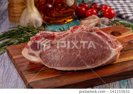 Raw pork chop on wooden cutting board with rosemary garlic and cherry tomatoes Raw pork chop on wooden cutting board with rosemary garlic and cherry tomatoes 141155632