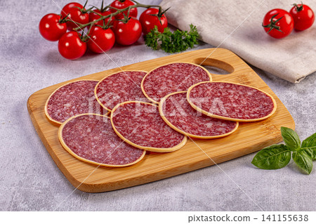 Sliced salami on wooden cutting board with cherry tomatoes and basil 141155638